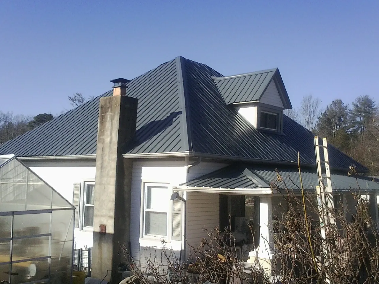 Dark blue standing seam metal roof on a white farmhouse with dormer — Slate & Tile Roof Repair by Roofing Brothers in Beltrami