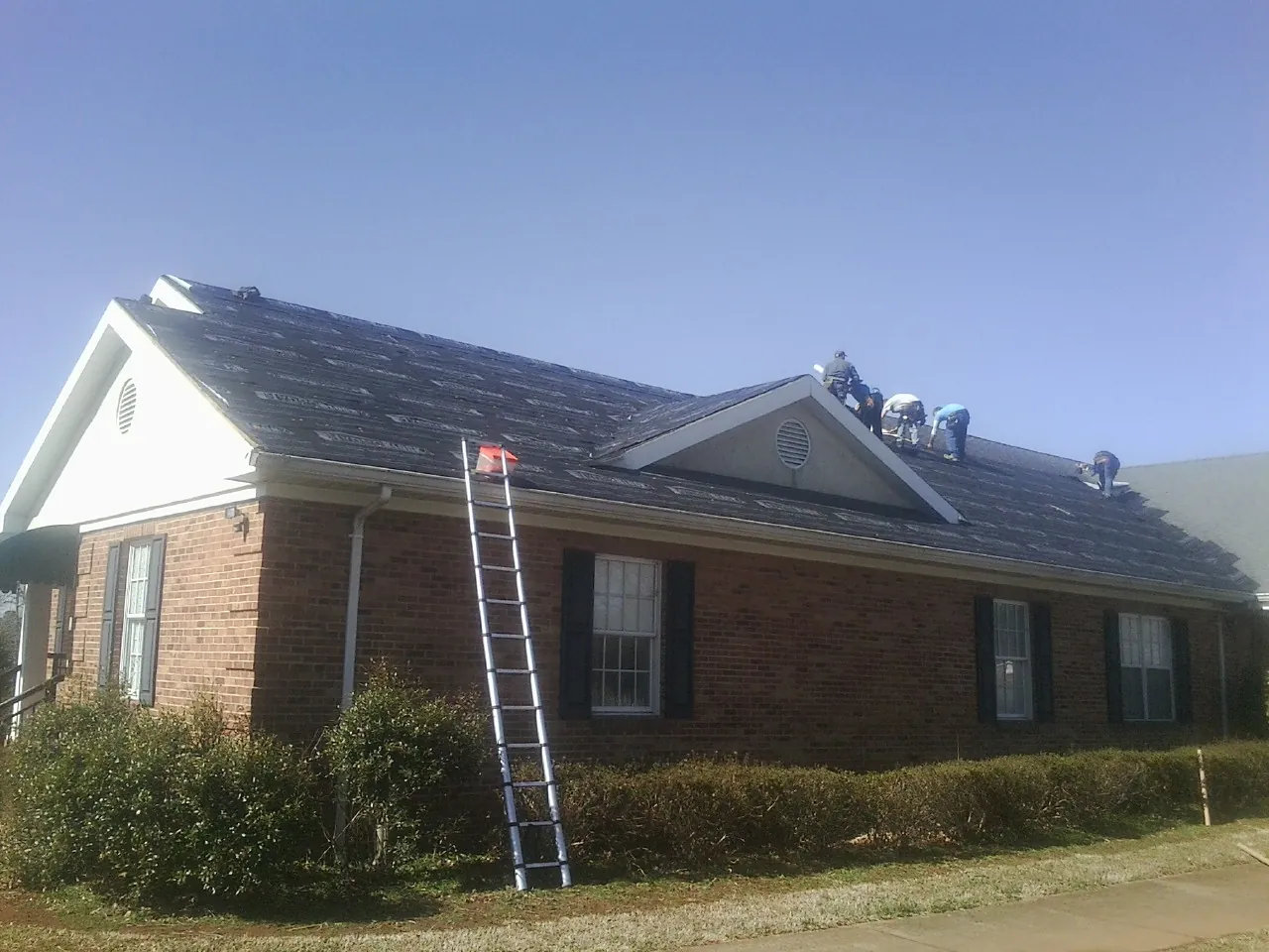 Crew tearing shingles off a brick ranch roof with a ladder set — Metal Roof Repair work by our crew in Beltrami