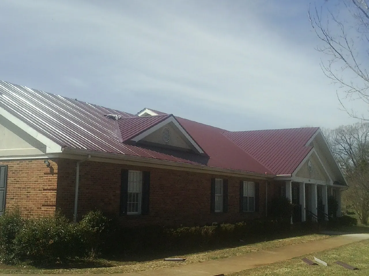 Red metal roof with gabled entries on a long brick building, from a Hail Damage Roof Repair job in Beltrami