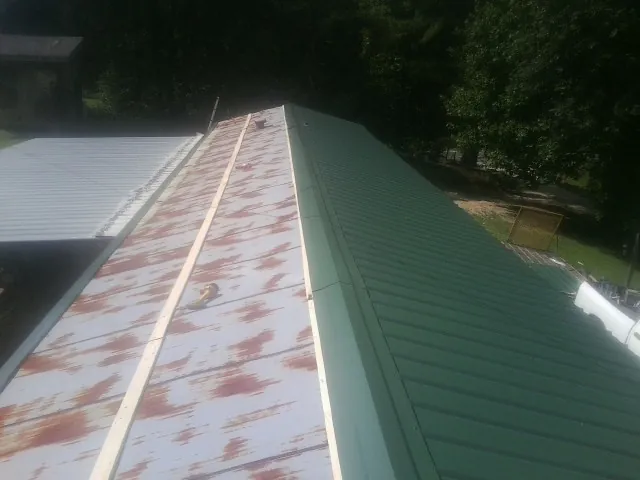 Old rusted panels beside newly installed green metal roofing — Wind Damage Roof Repair by Roofing Brothers in Beltrami