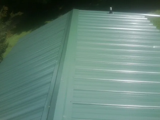 New green metal panels meeting at the ridge of a roof — Flat Roof Repair work by our crew in Beltrami