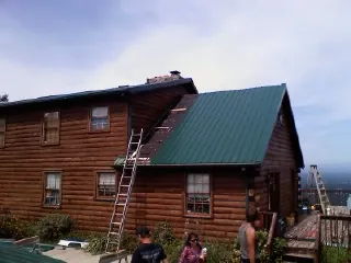 Green metal roof going on a two story log home with ladders set in Beltrami