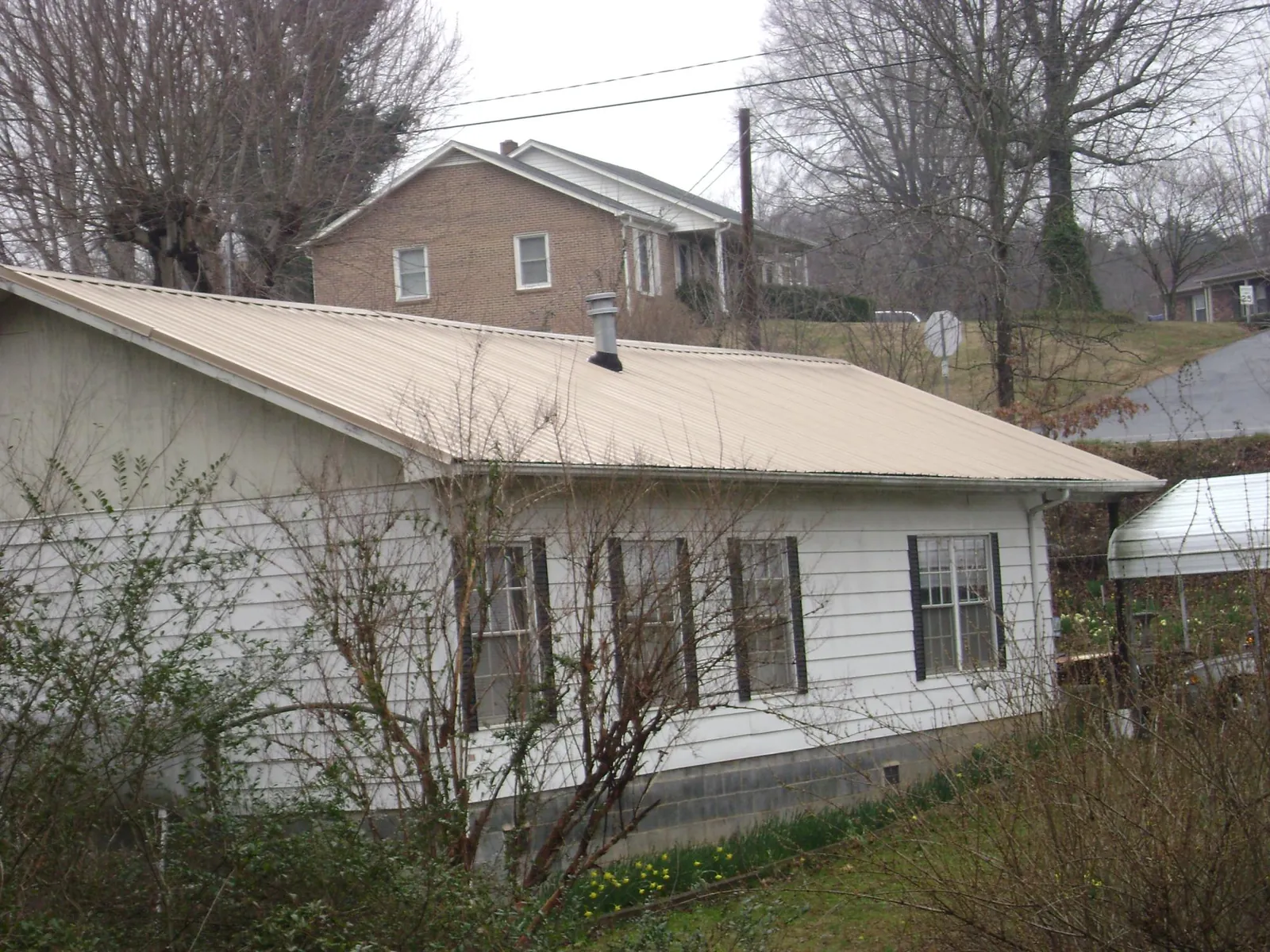 Tan metal roof on a white sided house set into a hillside — Commercial Roofing by Roofing Brothers in Beltrami