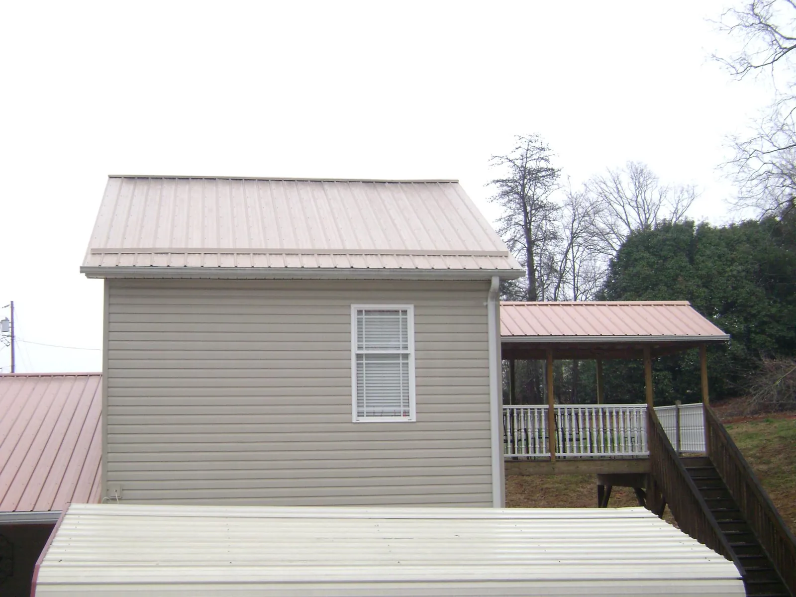 Tan metal roofs on a two story addition and attached porch, from a Roof Replacement job in Beltrami